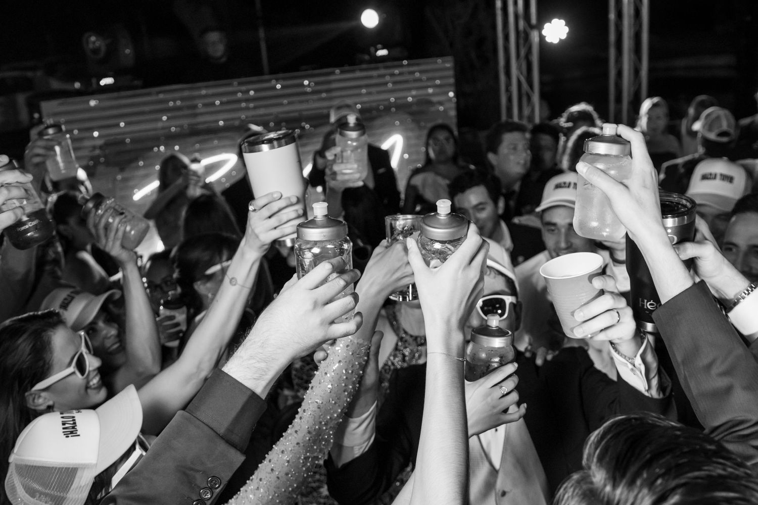 Crowd raises hands in celebration during nighttime party captured in black and white. Boda en Parras Coahuila, Fotógrafo de bodas