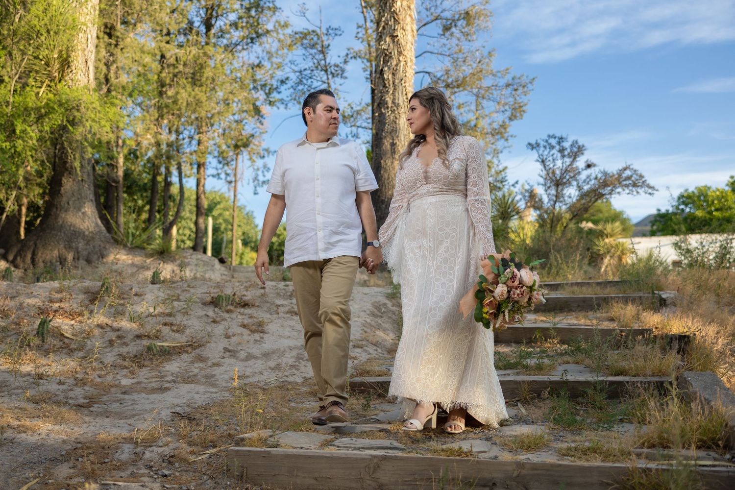 A couple walking hand in hand through a wooded area wearing casual and formal attire. Sesión en Parras Coahuila