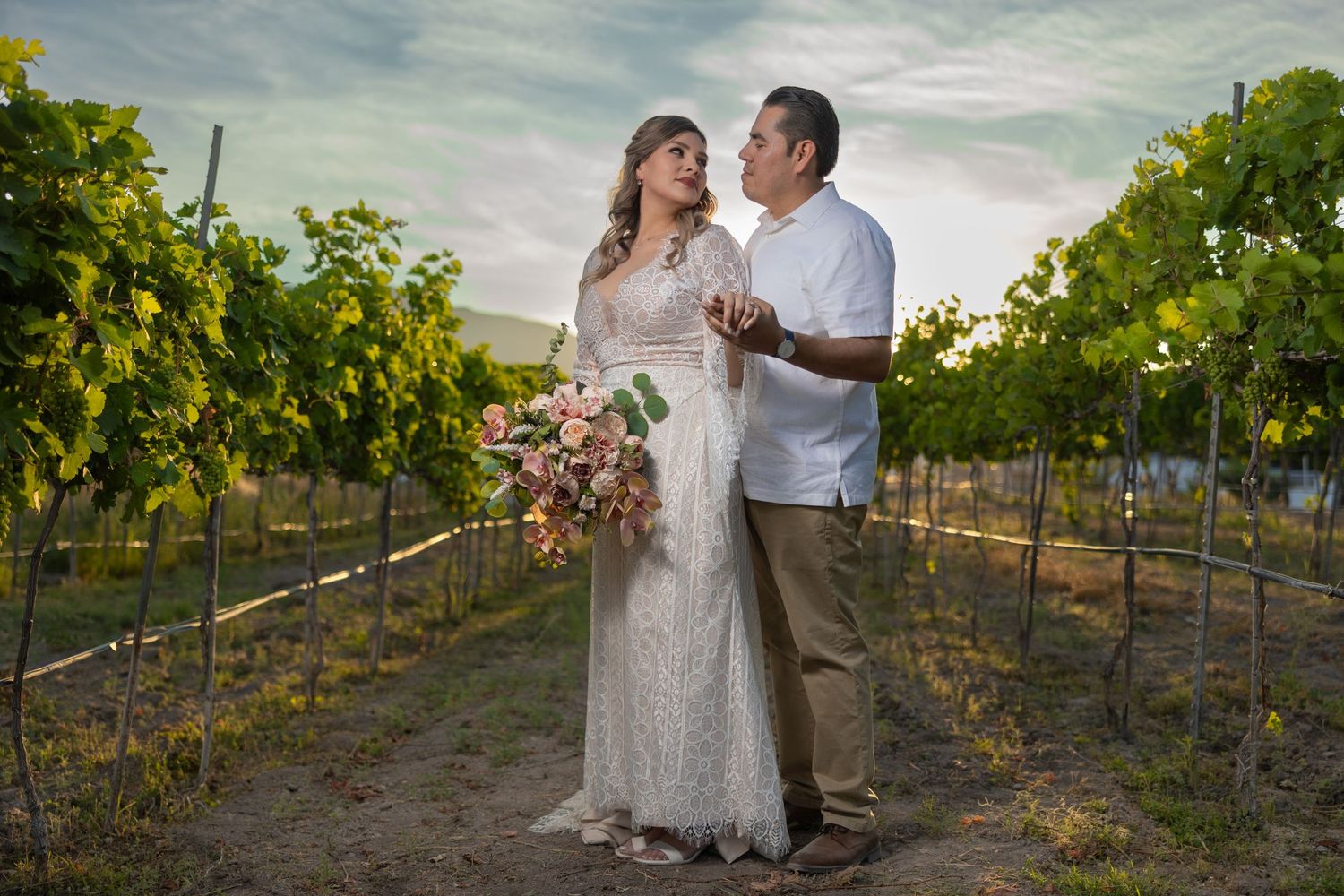 A romantic couple poses between rows of grapevines at dusk. boda en Parras Coahuila fotógrafo