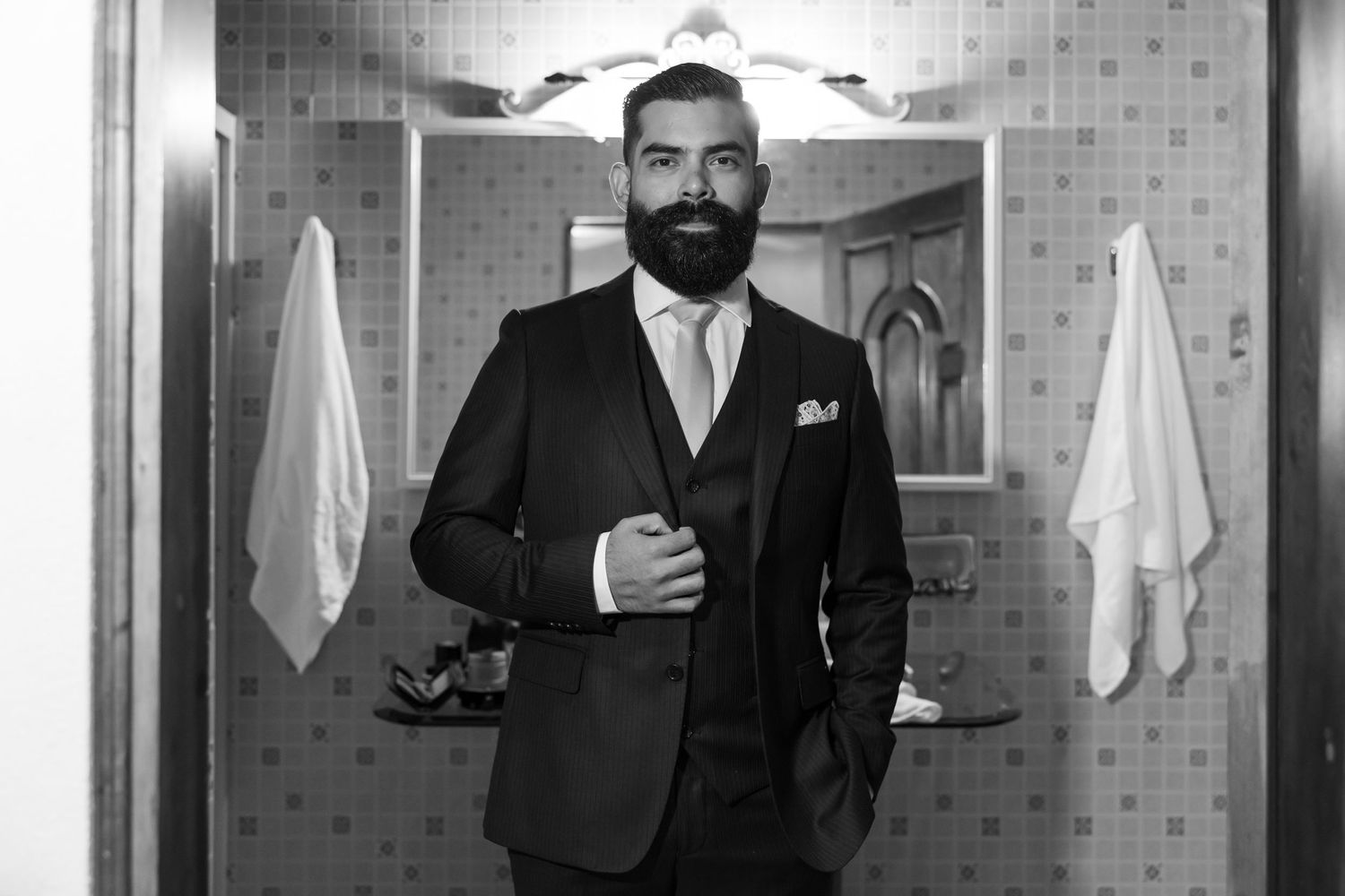A formal black and white portrait of a groom in a dark suit in a bathroom setting. Boda en Parras Coahuila, Fotógrafo de bodas