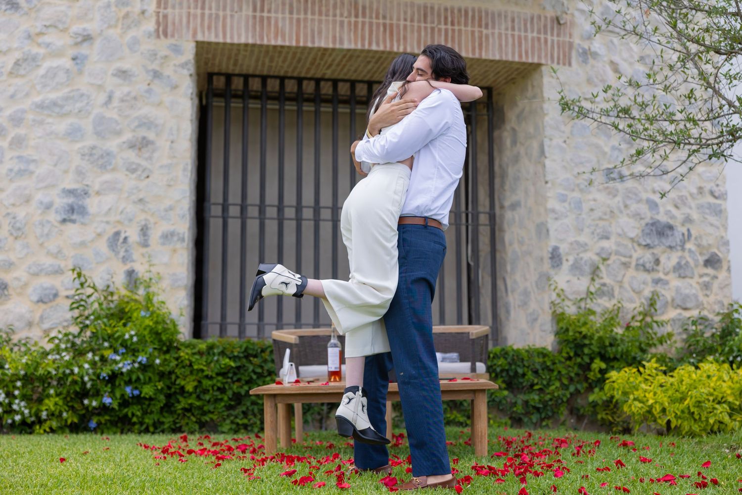 A joyful celebration embrace after a proposal with rose petals and a stone wall backdrop. Propuesta de matrimonio Parras, Fotografo