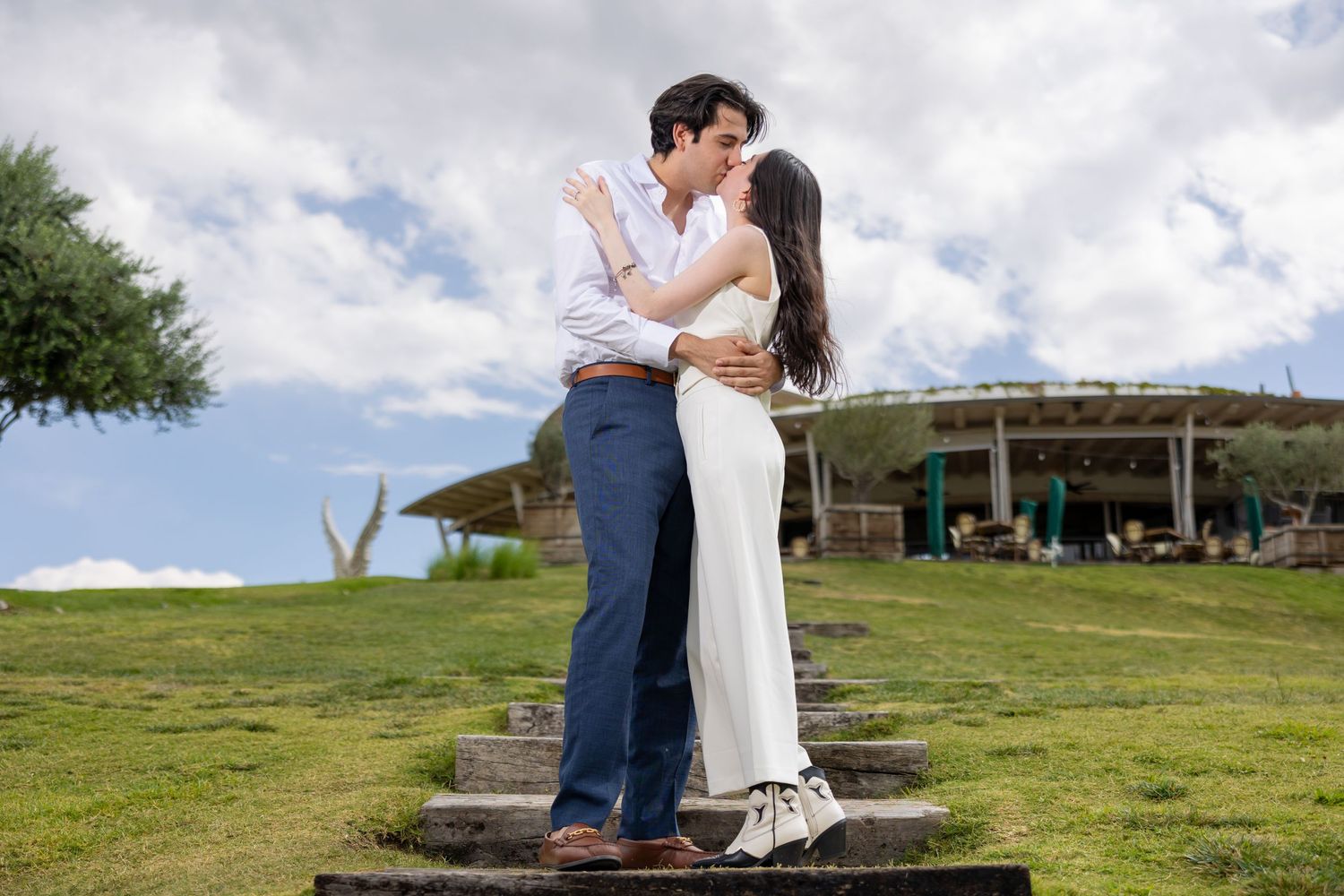 A romantic embrace on outdoor steps with a cloudy sky and building in the background. Propuesta de matrimonio Parras, Fotografo