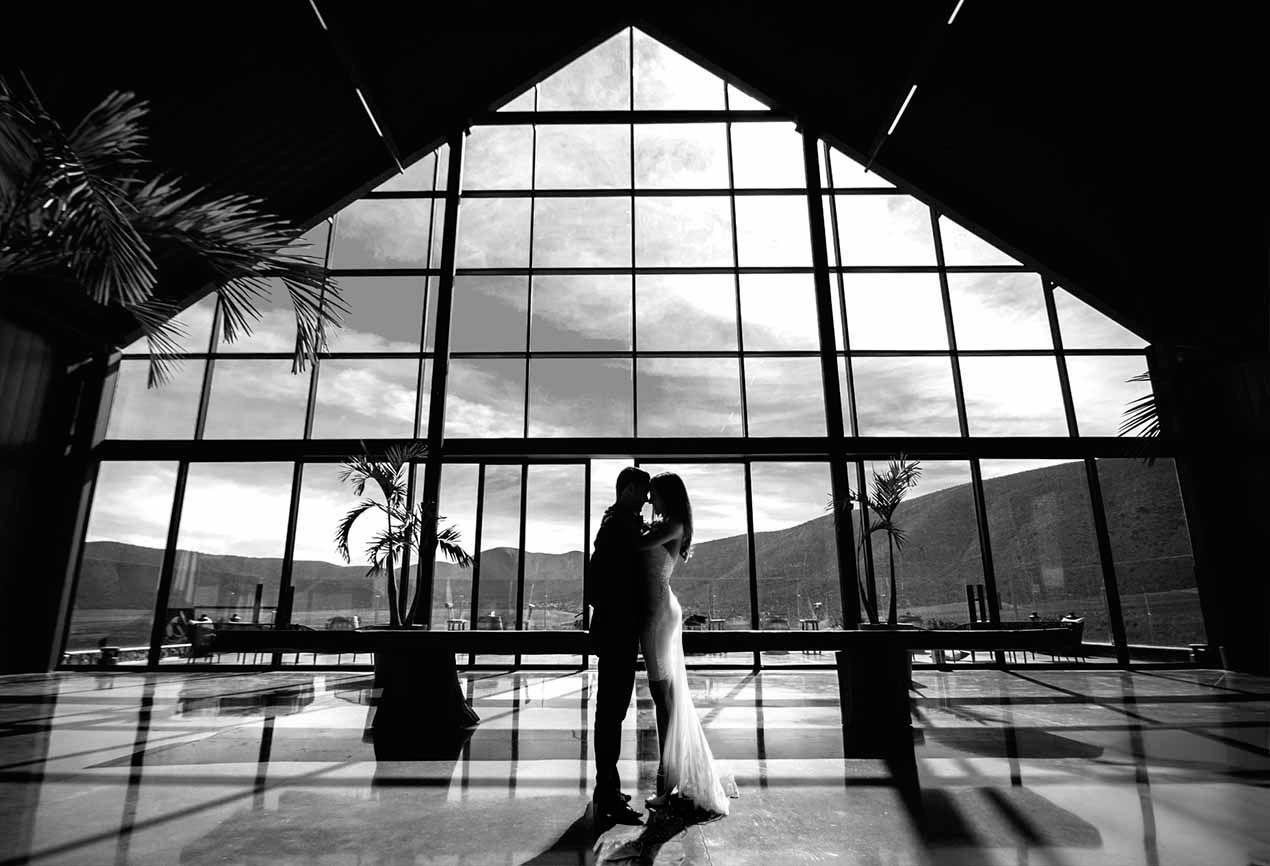 Silhouetted couple against dramatic geometric window architecture in black and white. boda en Parras Coahuila fotógrafo