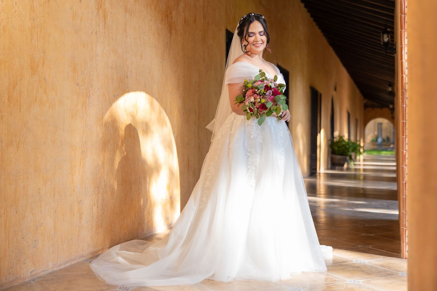 A bride in a flowing white gown poses in a sunlit Spanish colonial corridor. Boda en Parras Coahuila, Fotógrafo de bodas