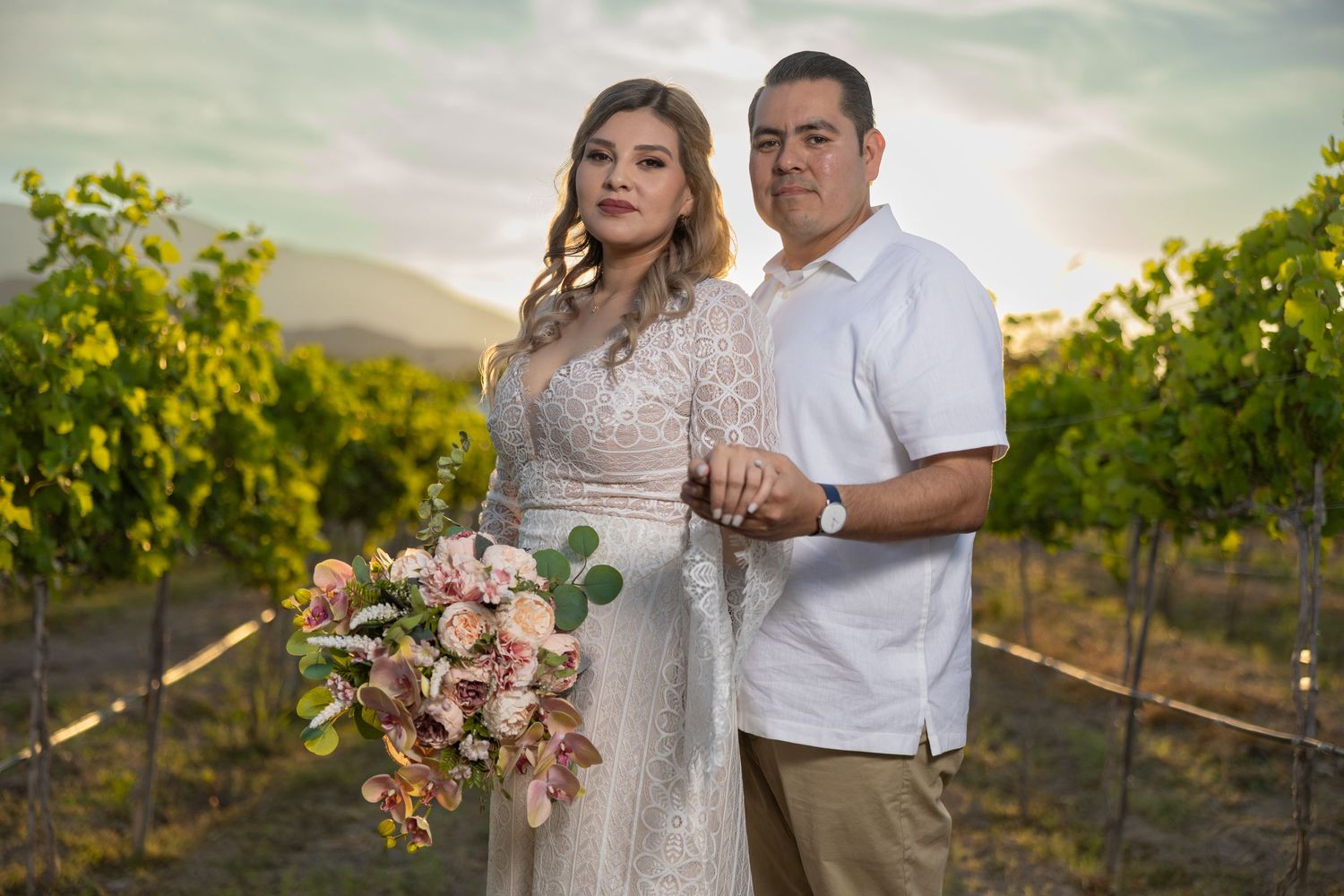 A couple poses in a vineyard at sunset holding a pink bouquet. Sesión en Parras Coahuila