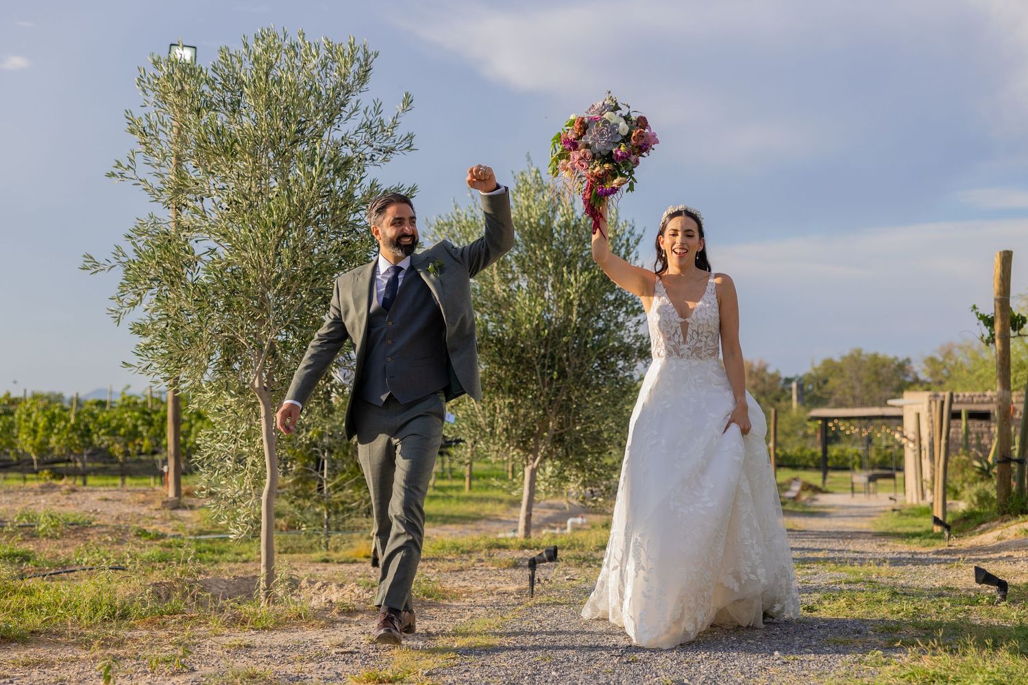 Newlyweds celebrate joyfully while walking down a path surrounded by desert landscape. Boda en Parras Coahuila fotógrafo