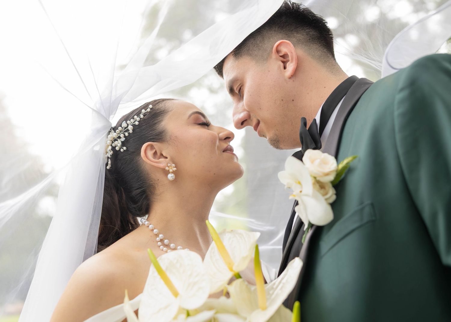 A romantic wedding couple shares an intimate moment surrounded by soft lighting and white calla lily flowers.