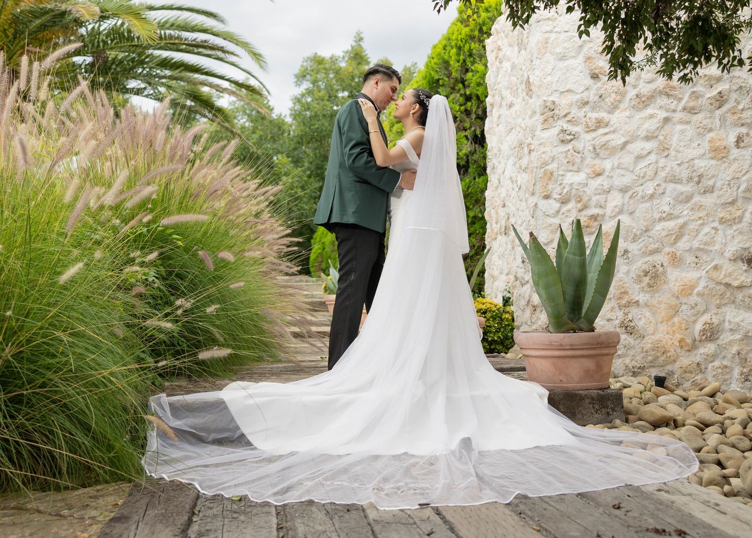 A couple shares a romantic moment in a garden setting with stone walls, palm trees and ornamental grasses.