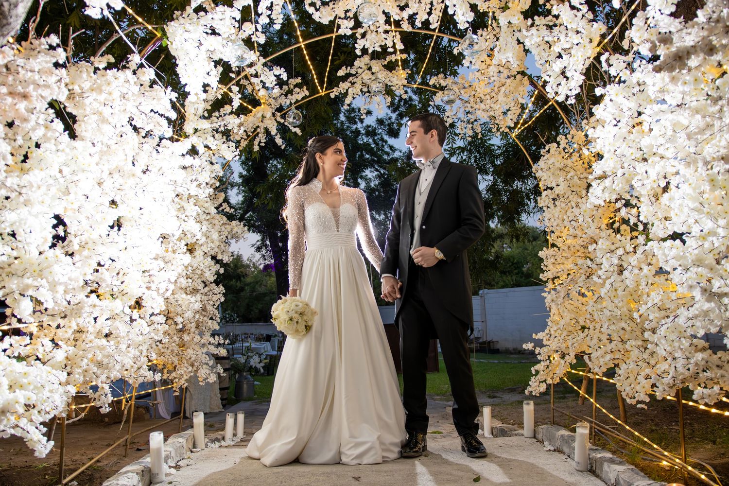 A wedding ceremony setup with an elegant floral arch filled with white cherry blossoms. Boda en Parras Coahuila fotógrafo