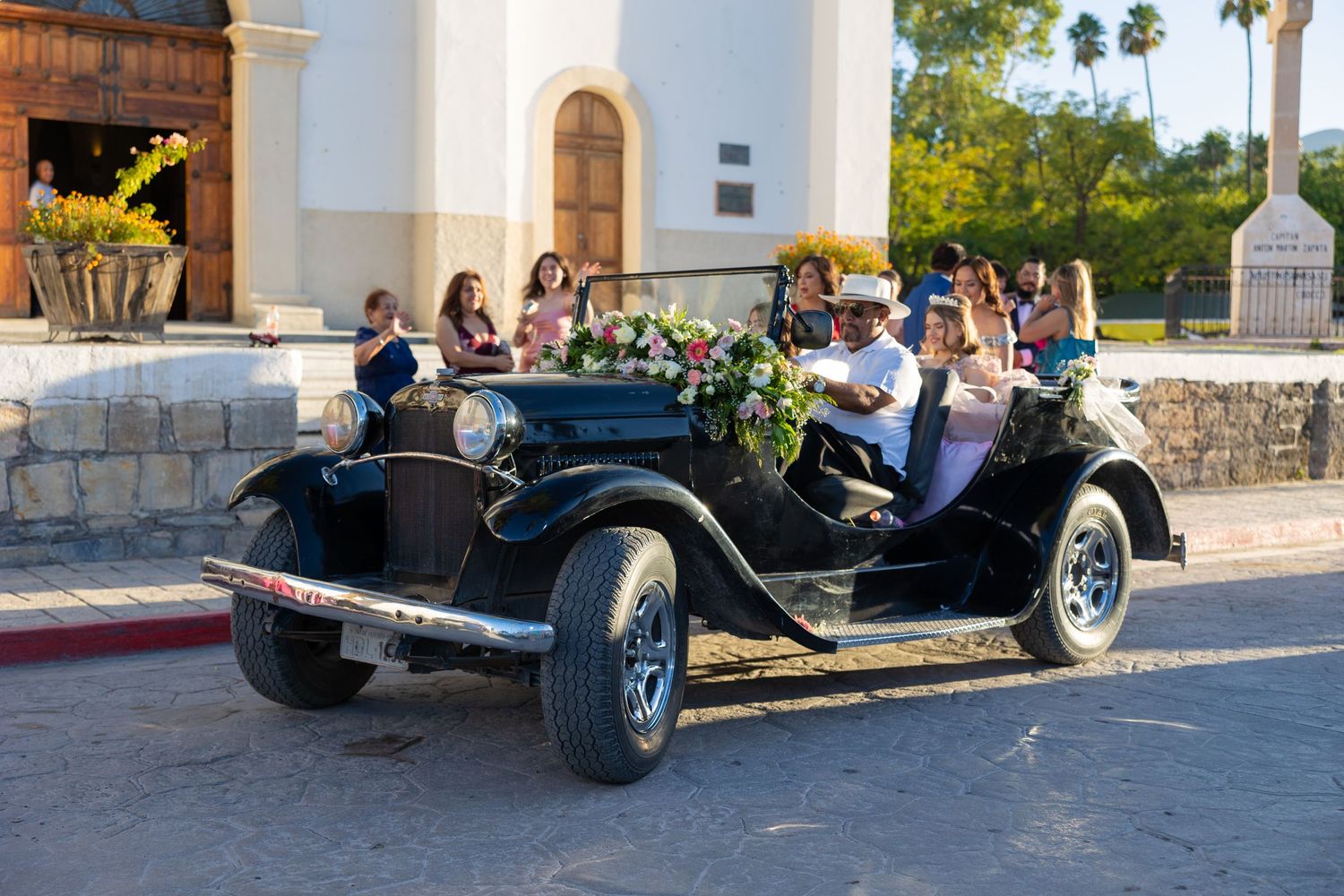 Classic black vintage car parked outside white church building with palm trees. Evento en Parras Coahuila , Fotógrafo Rulo