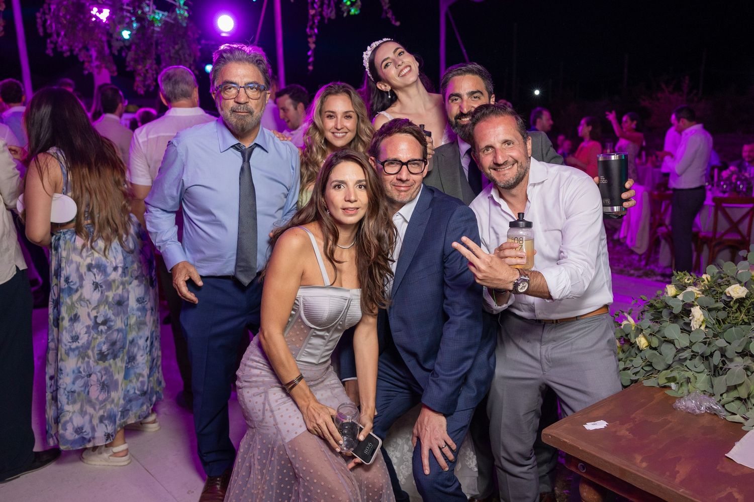 Wedding celebration group photo with party guests under purple ambient lighting. Boda en Parras Coahuila fotógrafo