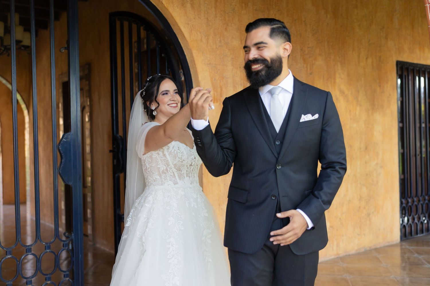 A couple shares a joyful moment against a yellow stucco wall during their wedding. Boda en Parras Coahuila, Fotógrafo de bodas
