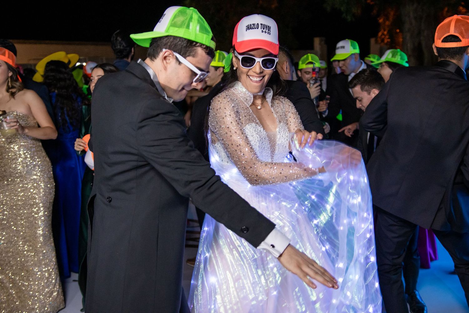 Wedding guests dance while wearing colorful baseball caps at an evening reception. Boda en Parras Coahuila, Fotógrafo de bodas