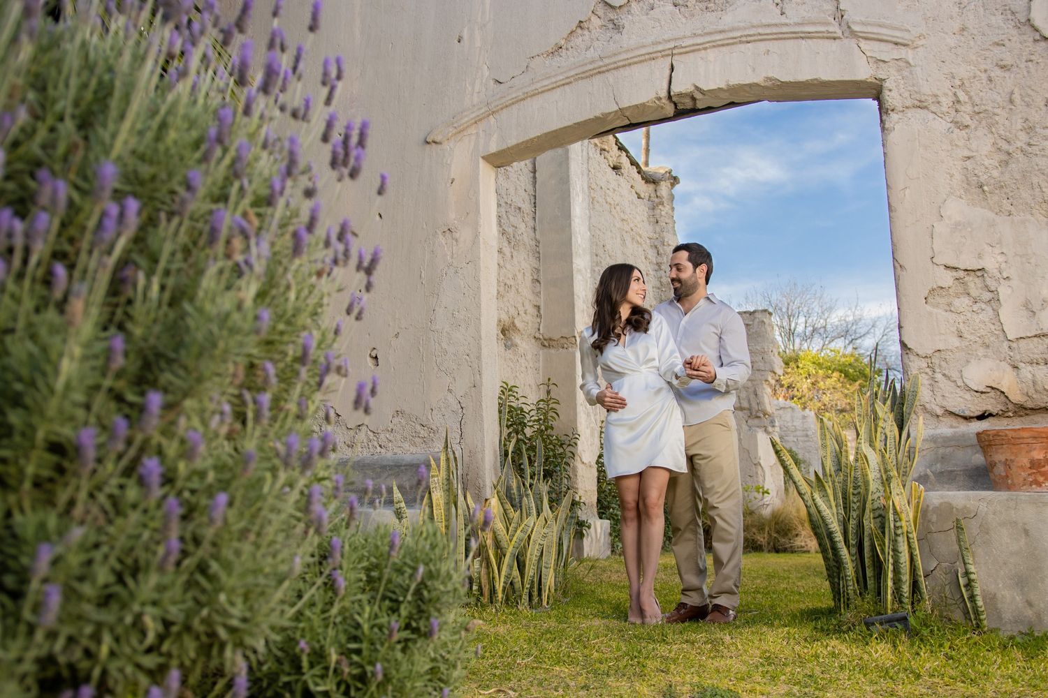 Couple standing in stone archway surrounded by lavender and garden flowers. Boda en Parras Coahuila fotógrafo