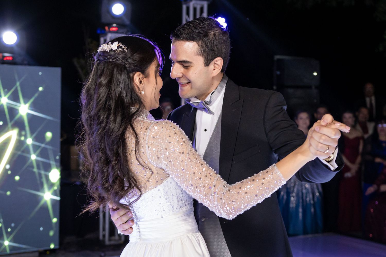 Newlyweds share an intimate dance moment on a lit stage with sparkling decorative elements in the background. Boda en Parras Coahuila, Foto