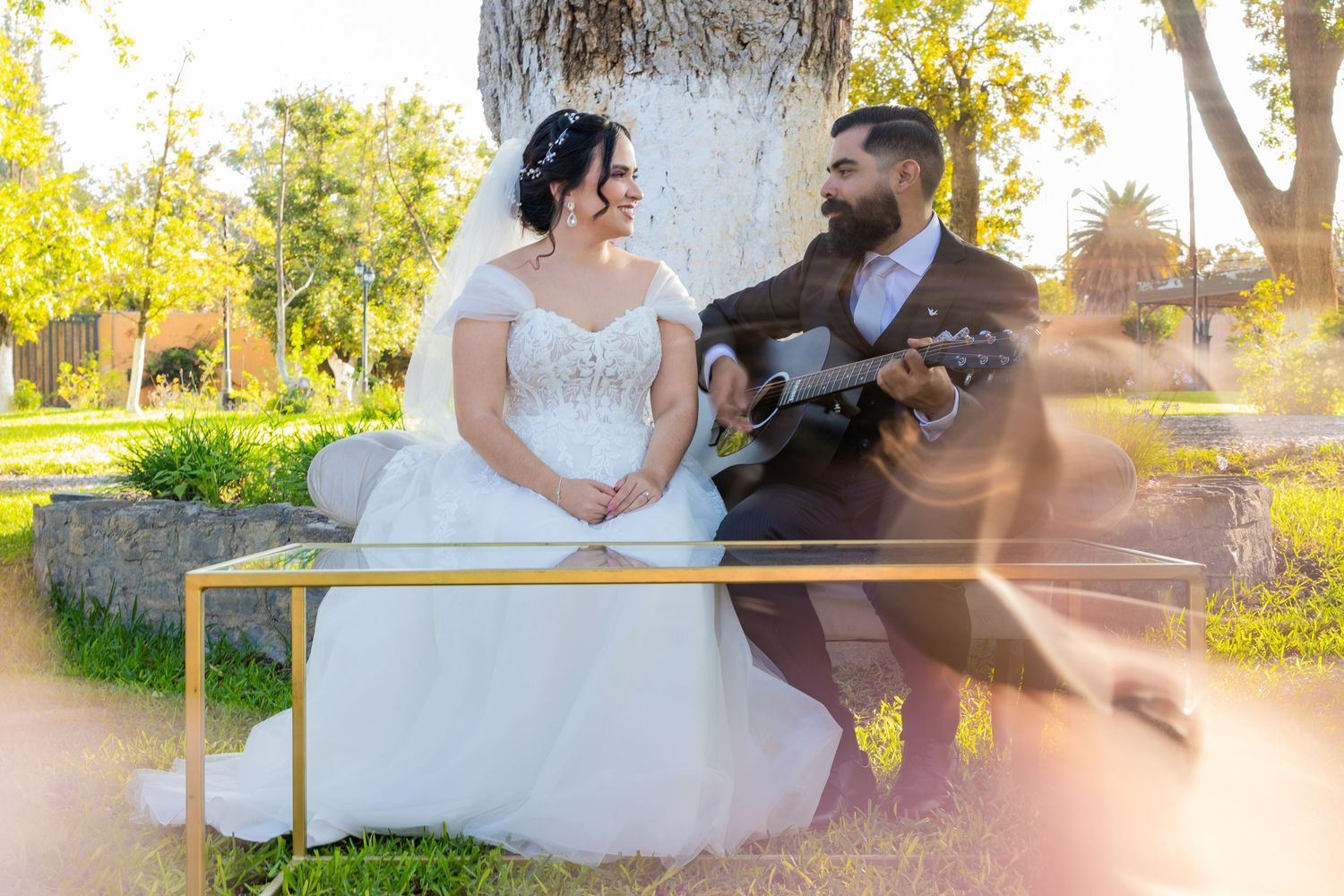 A couple shares a musical moment on a bench in wedding attire during golden hour. Boda en Parras Coahuila, Fotógrafo de bodas