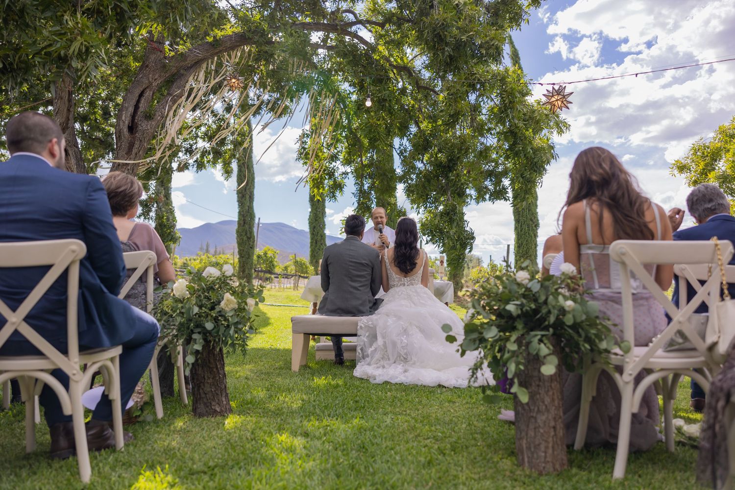 Outdoor wedding ceremony with guests seated facing couple under tree canopy. Boda en Parras Coahuila fotógrafo