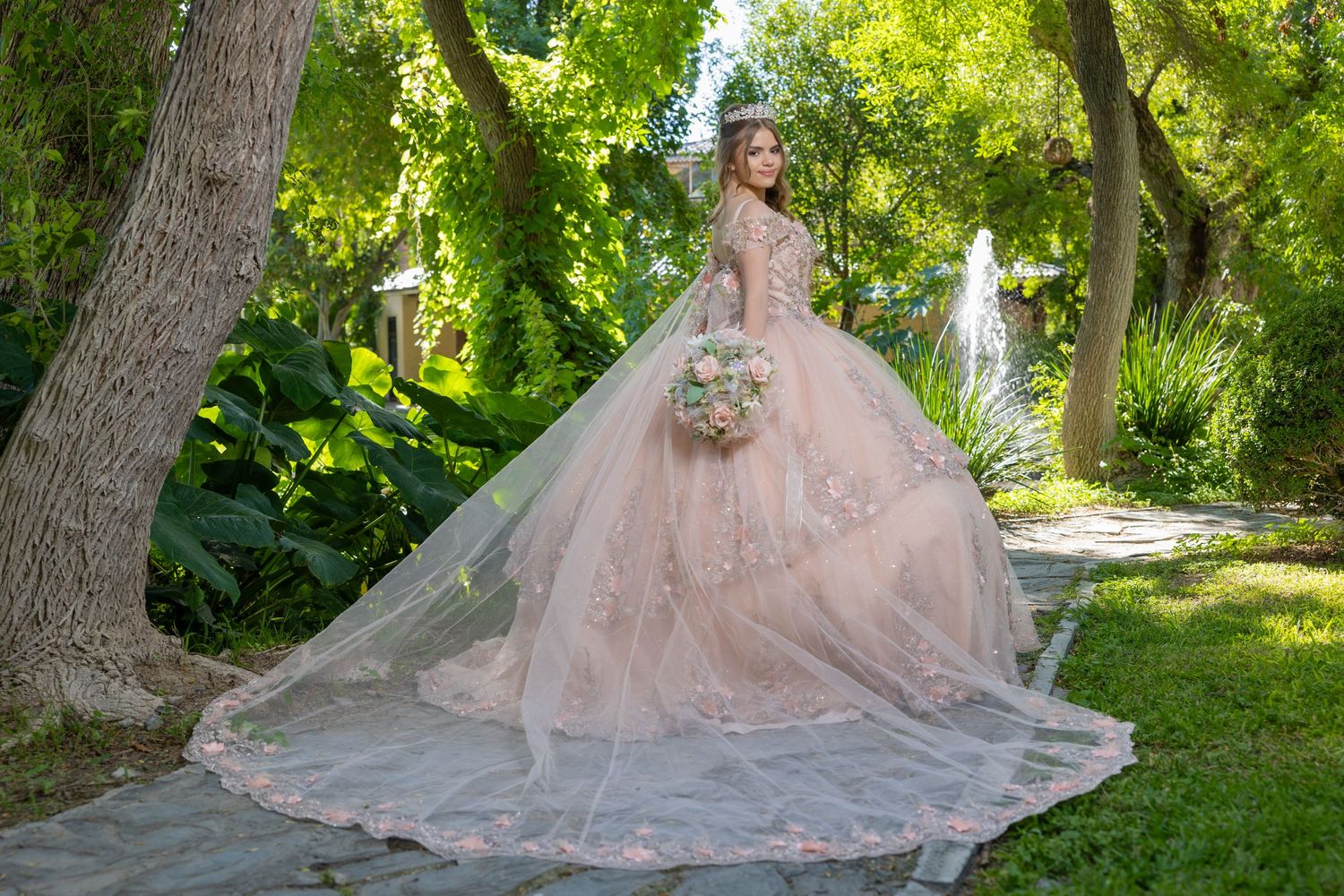 A luxurious pink ball gown with extensive train photographed against green garden scenery. Evento en Parras Coahuila , Fotógrafo Rulo