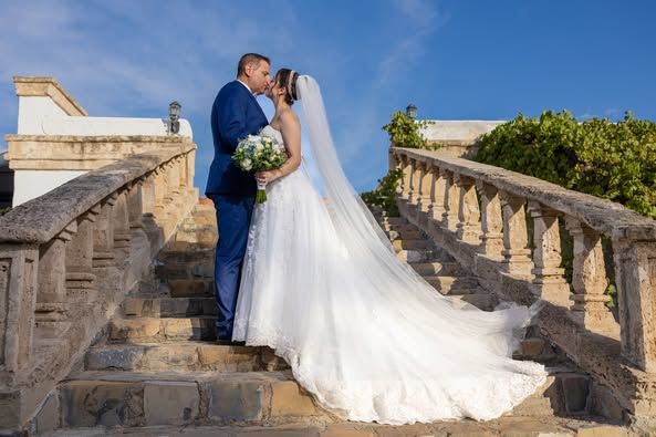 A romantic wedding portrait on historic stone steps with flowing white dress and clear blue sky. Boda en Parras Coahuila fotógrafo