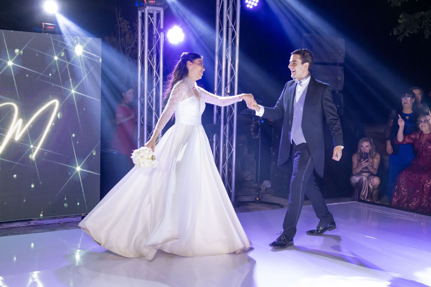 A couple performs their first dance on an illuminated stage with dramatic lighting and theatrical effects. Boda en Parras Coahuila, Foto