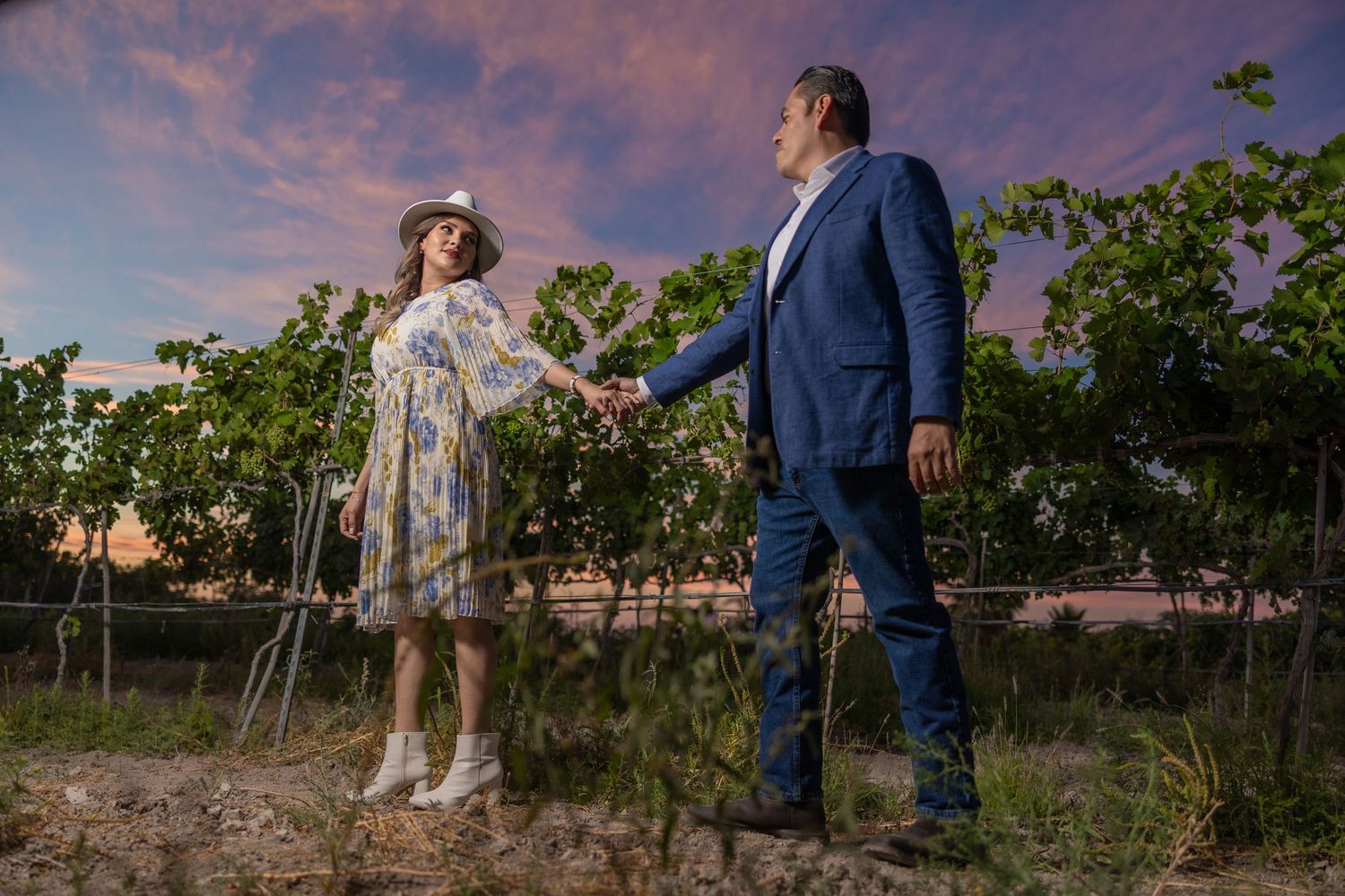 Couple holds hands in vineyard with dramatic sunset sky above. boda en Parras Coahuila fotógrafo