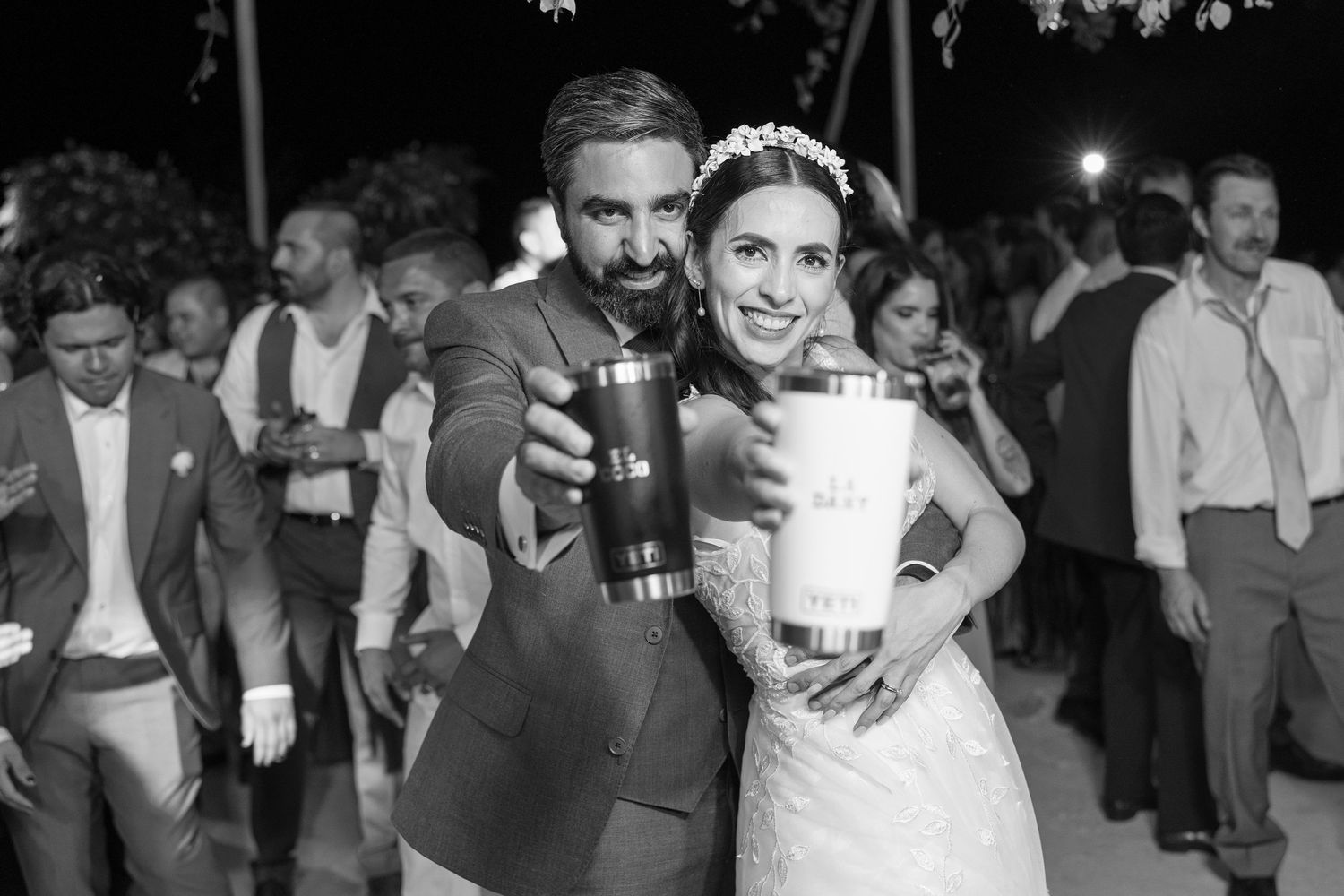 Black and white photo of newlyweds posing together with drinks at outdoor reception. Boda en Parras Coahuila fotógrafo