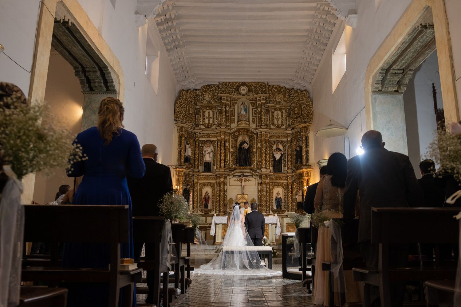 Interior view of a traditional church with ornate golden altars and pews illuminated by natural light through windows.