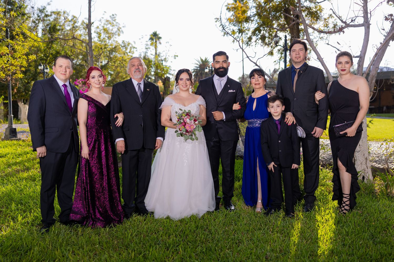 A wedding party in formal attire poses together on grass with trees in the background. Boda en Parras Coahuila, Fotógrafo de bodas
