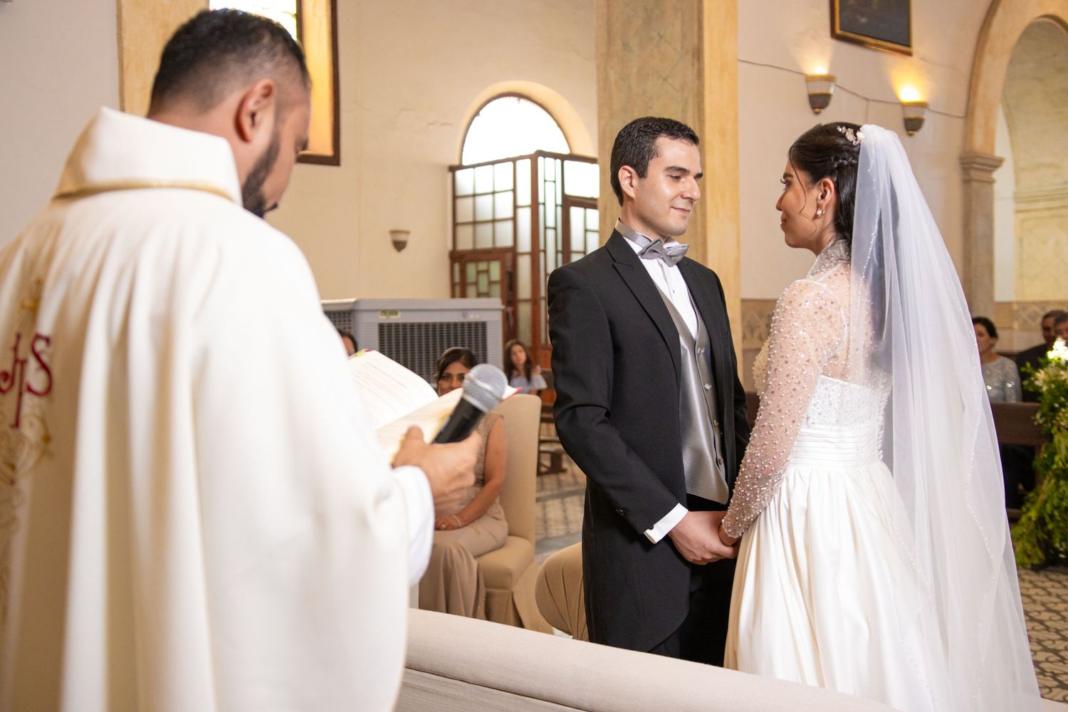 A Catholic priest conducts a traditional wedding ceremony in an ornate church with arched architecture. Boda en Parras Coahuila, Fotógrafo