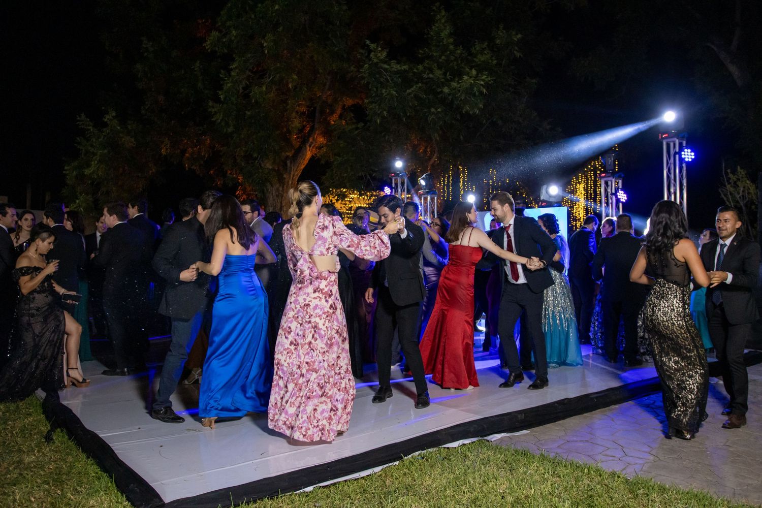 Dancers in formal gowns and suits celebrate on an outdoor dance floor under blue lighting.Boda en Parras Coahuila, Fotógrafo de bodas