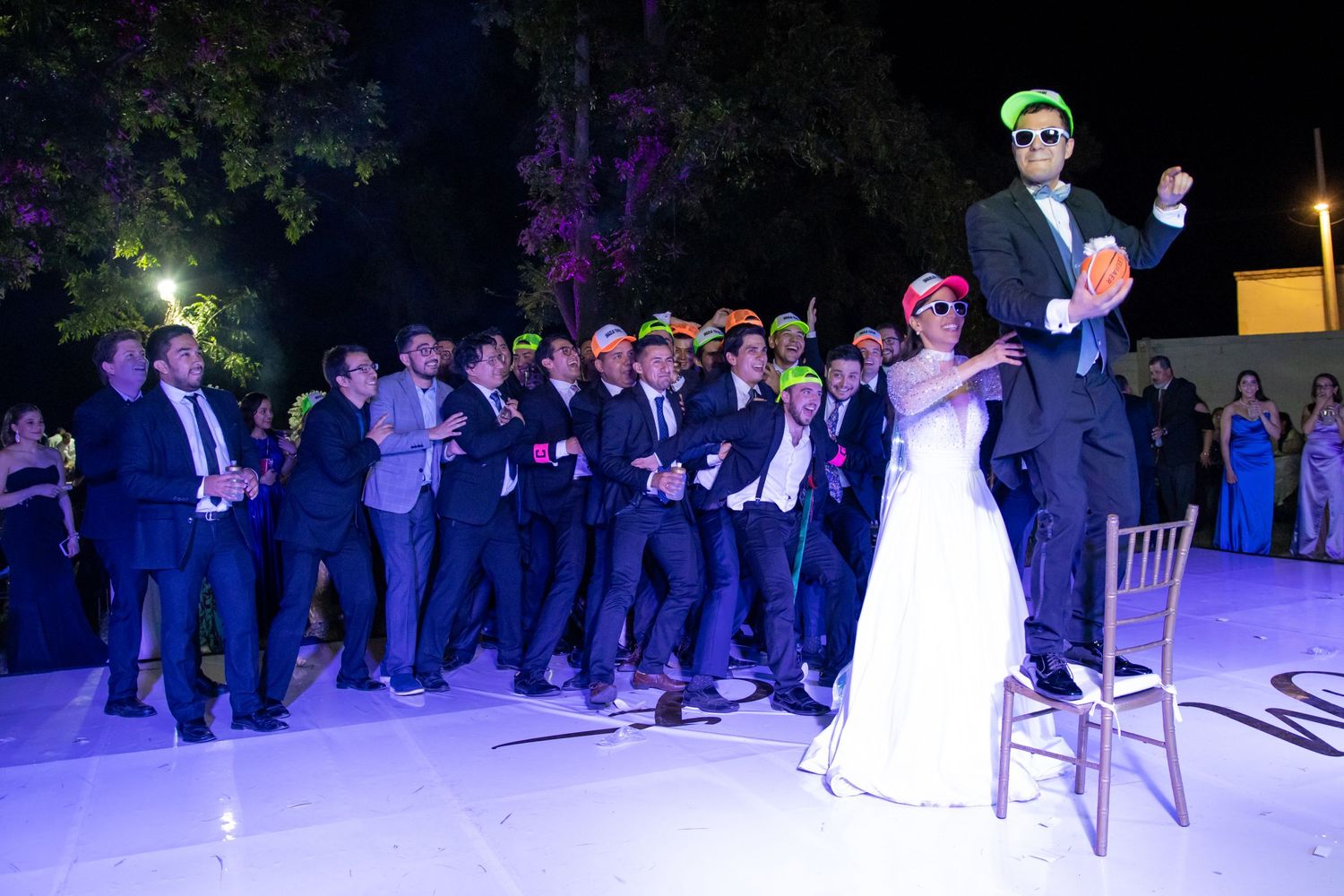 Wedding party members pose in formation on a lit dance floor during an outdoor evening celebration. Boda en Parras Coahuila, Fotógrafo