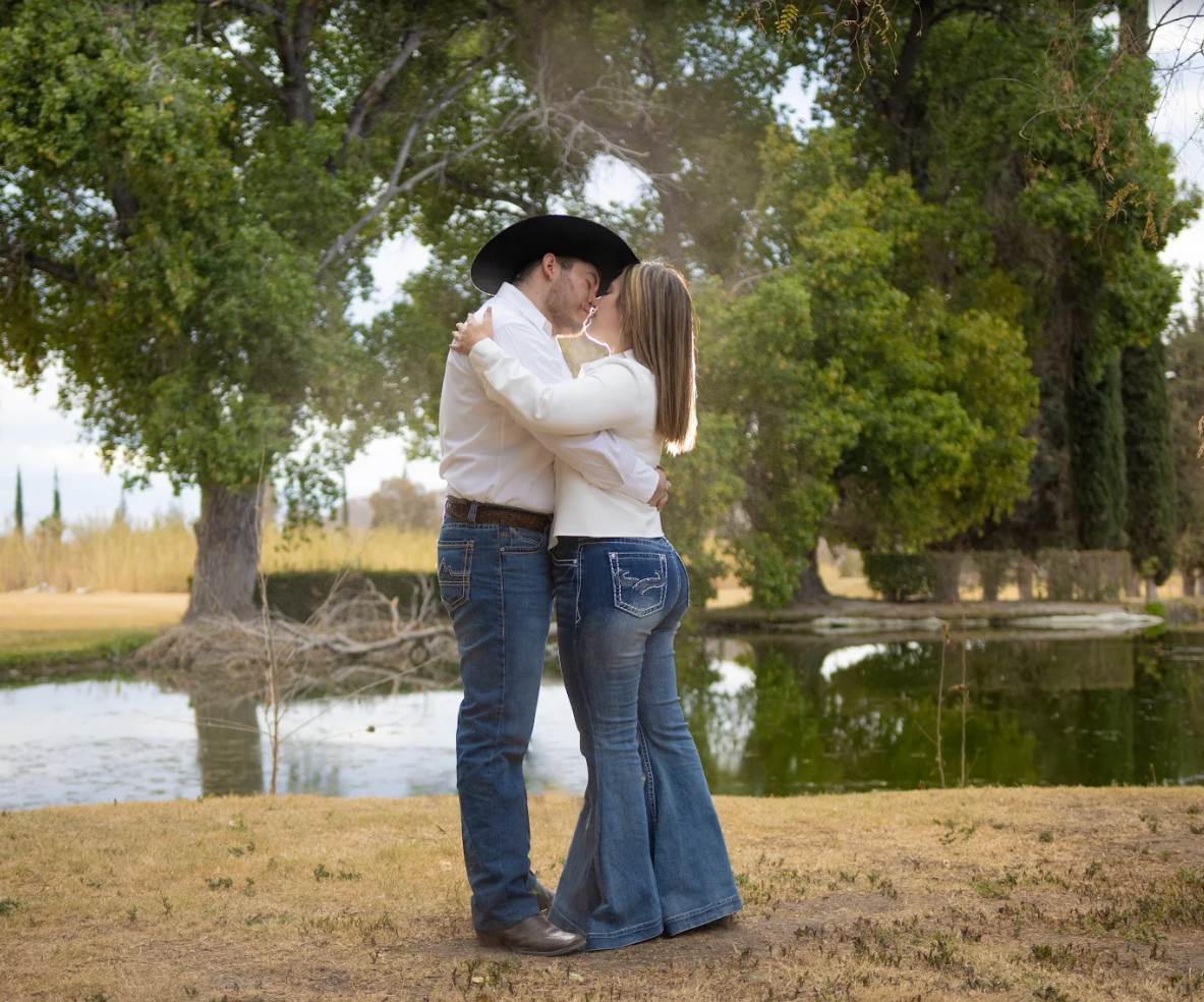 A romantic couple embracing under tall trees near a pond. boda en Parras Coahuila fotógrafo