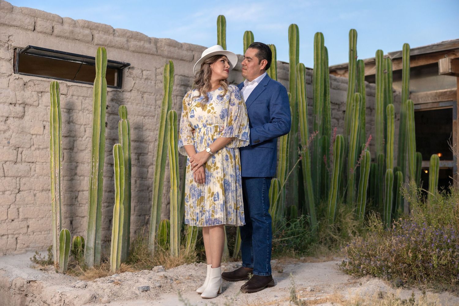 Couple stands among tall desert cactus near adobe wall in southwestern setting. boda en Parras Coahuila fotógrafo