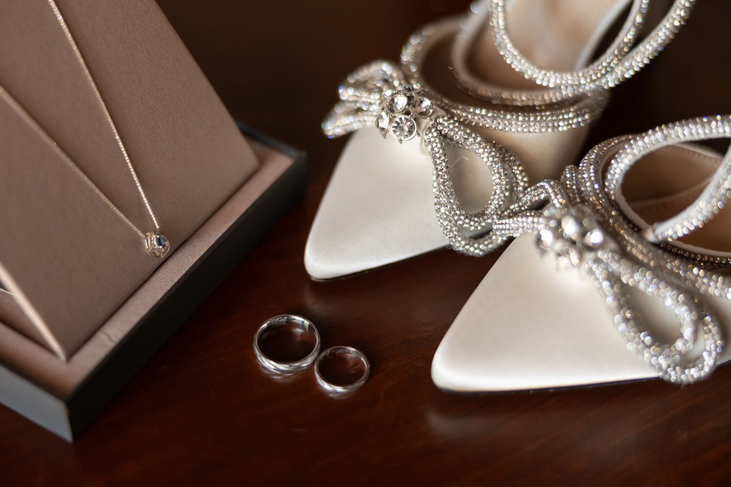 Elegant bridal accessories including white heels, jewelry, and wedding rings on a dark wood surface. Boda en Parras Coahuila fotógrafo