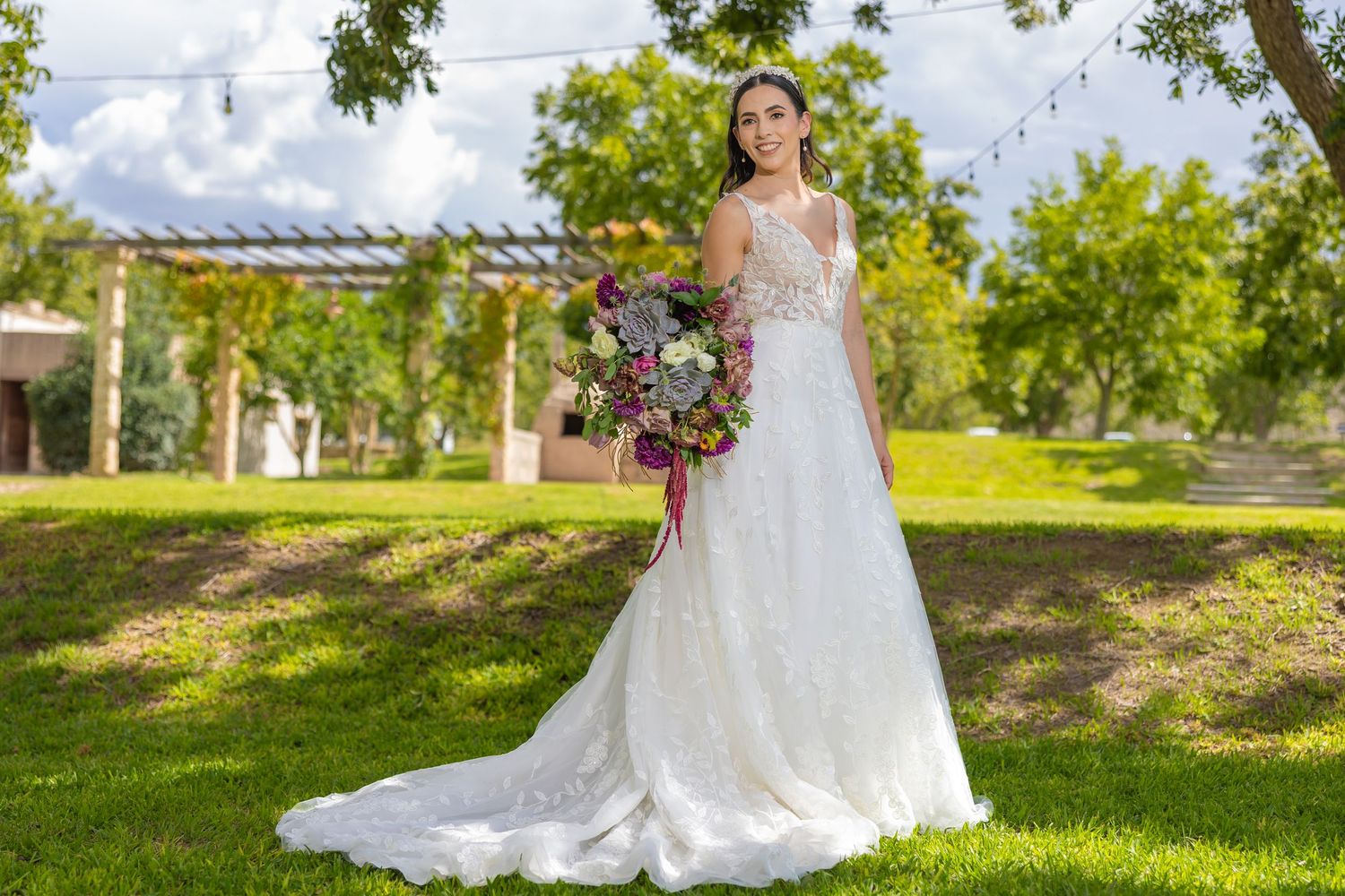 A wedding portrait featuring an elegant lace gown and vibrant purple bouquet in a garden setting. Boda en Parras Coahuila fotógrafo