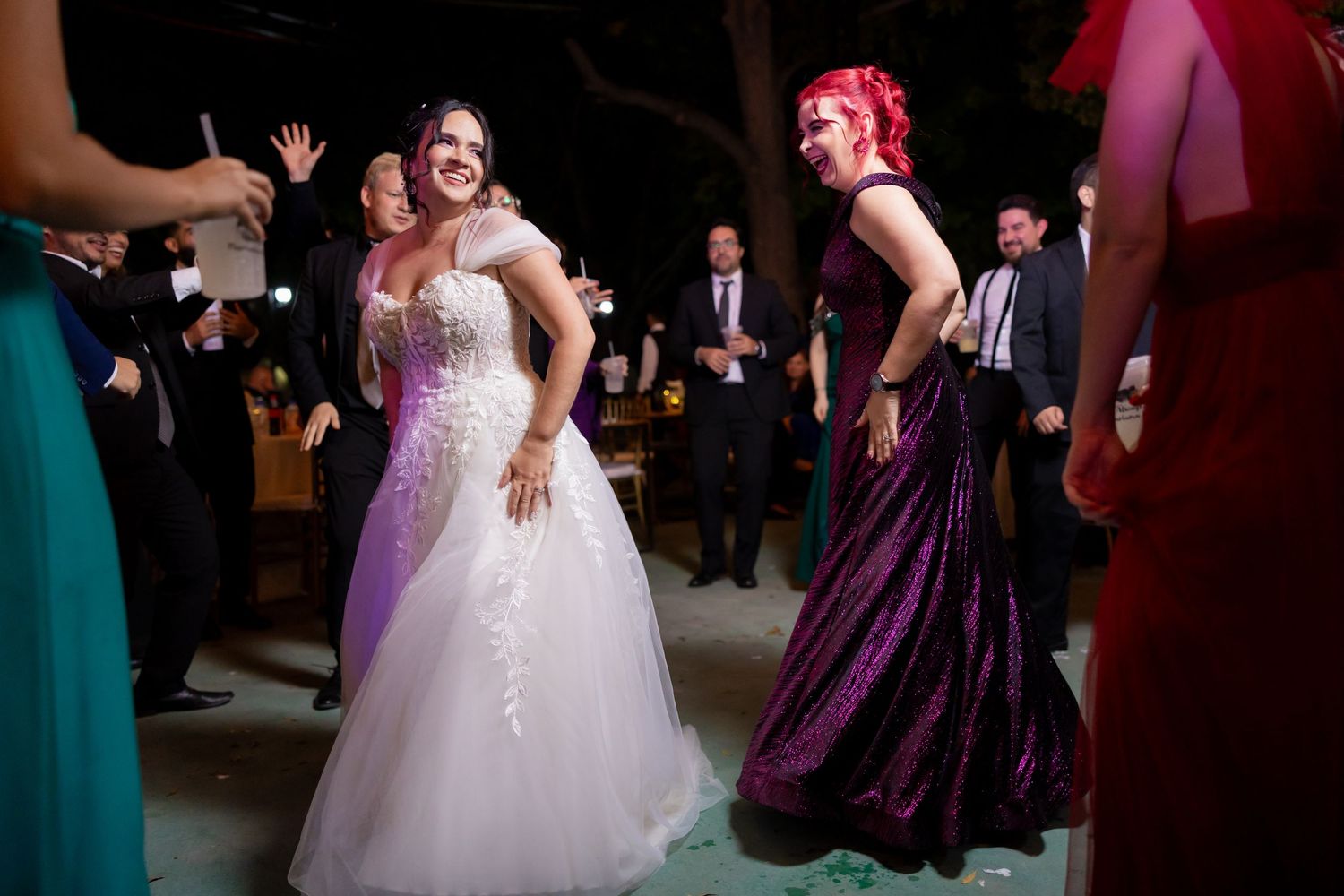 Bride in white gown dancing alongside guest in purple dress at reception. Boda en Parras Coahuila, Fotógrafo de bodas,