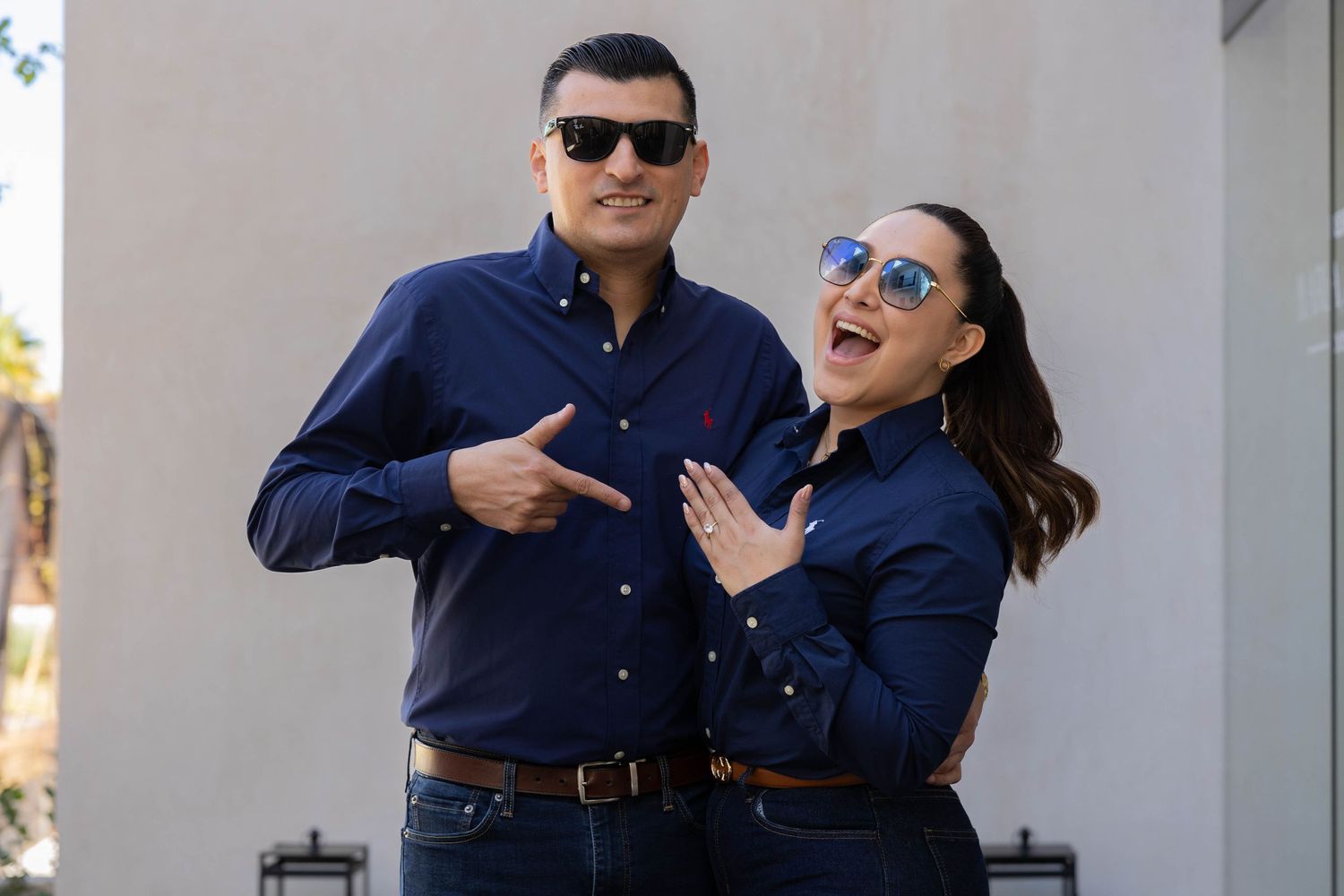 A couple in matching navy blue outfits laughs and poses together outdoors.
