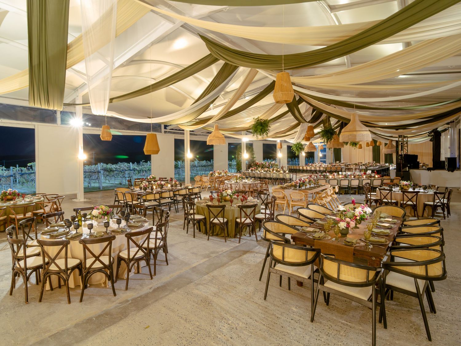 Elegant banquet hall with draped fabric ceiling, wooden cross-back chairs and tables set for a formal dining event.