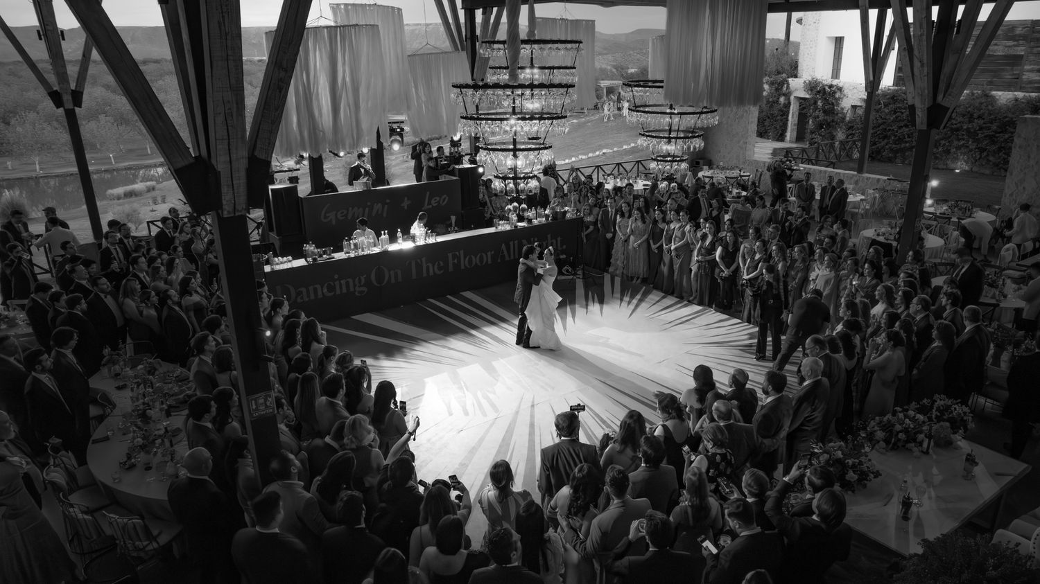 Black and white panoramic view of a large crowd gathered in an indoor event space with dramatic lighting.