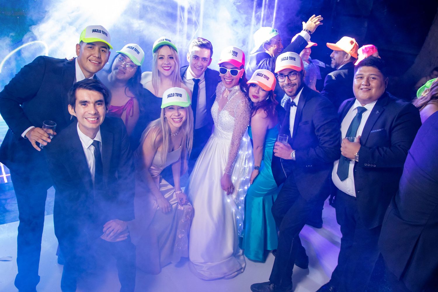 Large group poses together wearing party hats and formal attire with fog effects and blue lighting. Boda en Parras Coahuila, Fotógrafo de bo