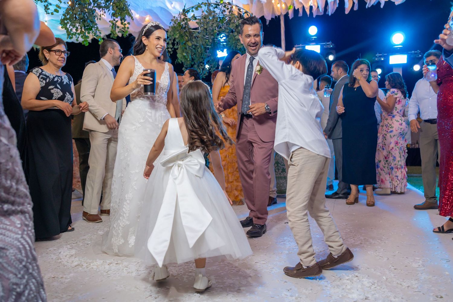 Wedding guests dancing joyfully on a decorated dance floor with blue lighting and hanging florals. Boda en Parras Coahuila fotógrafo