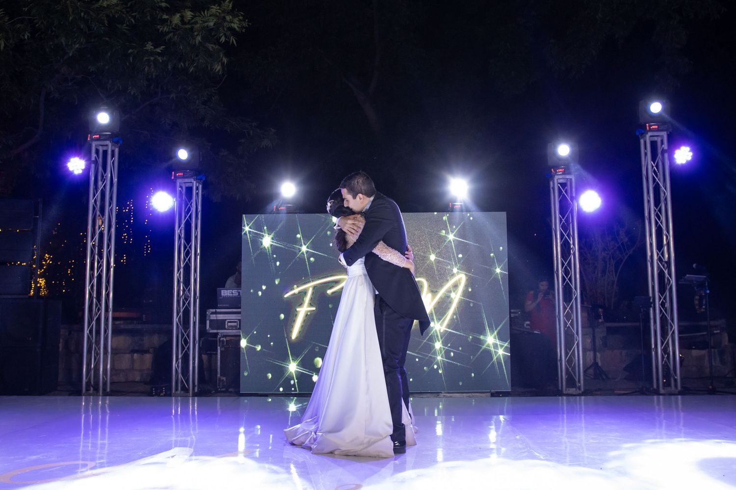Newlyweds dance together on a lit stage surrounded by blue theatrical lighting and star decorations. Boda en Parras Coahuila, Fotógrafo