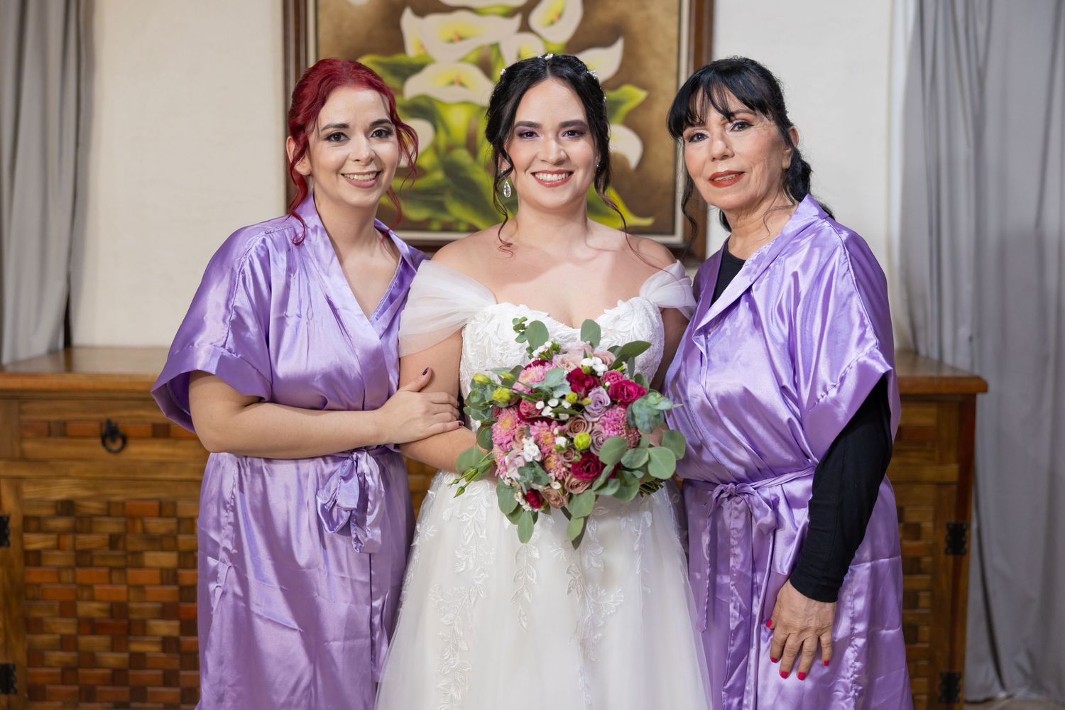 Three people in matching purple robes pose with a wedding bouquet during preparation. Boda en Parras Coahuila, Fotógrafo de bodas