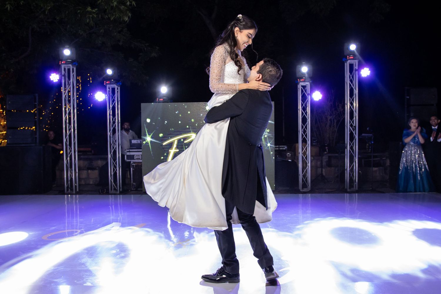A wedding couple performs a dramatic dance lift on a spotlit dance floor with purple stage lighting. Boda en Parras Coahuila, Fotógrafo