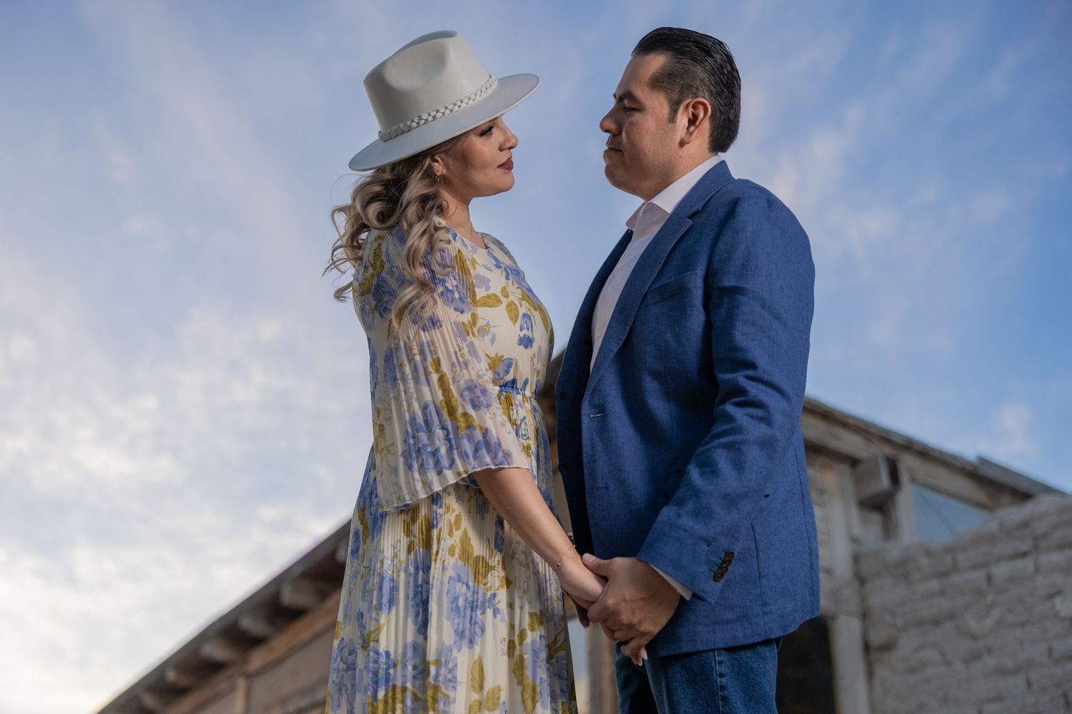 Couple in vintage attire poses against sky at twilight near rustic building. boda en Parras Coahuila fotógrafo