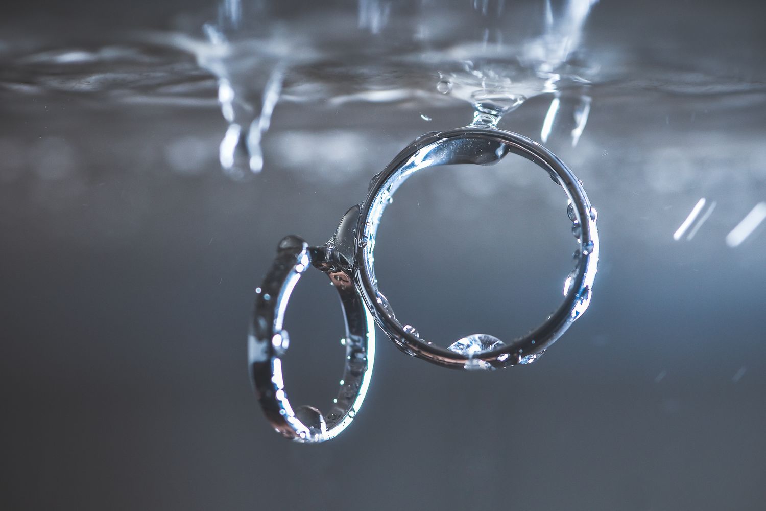 Two diamond wedding rings submerged in water with sparkling light reflections.