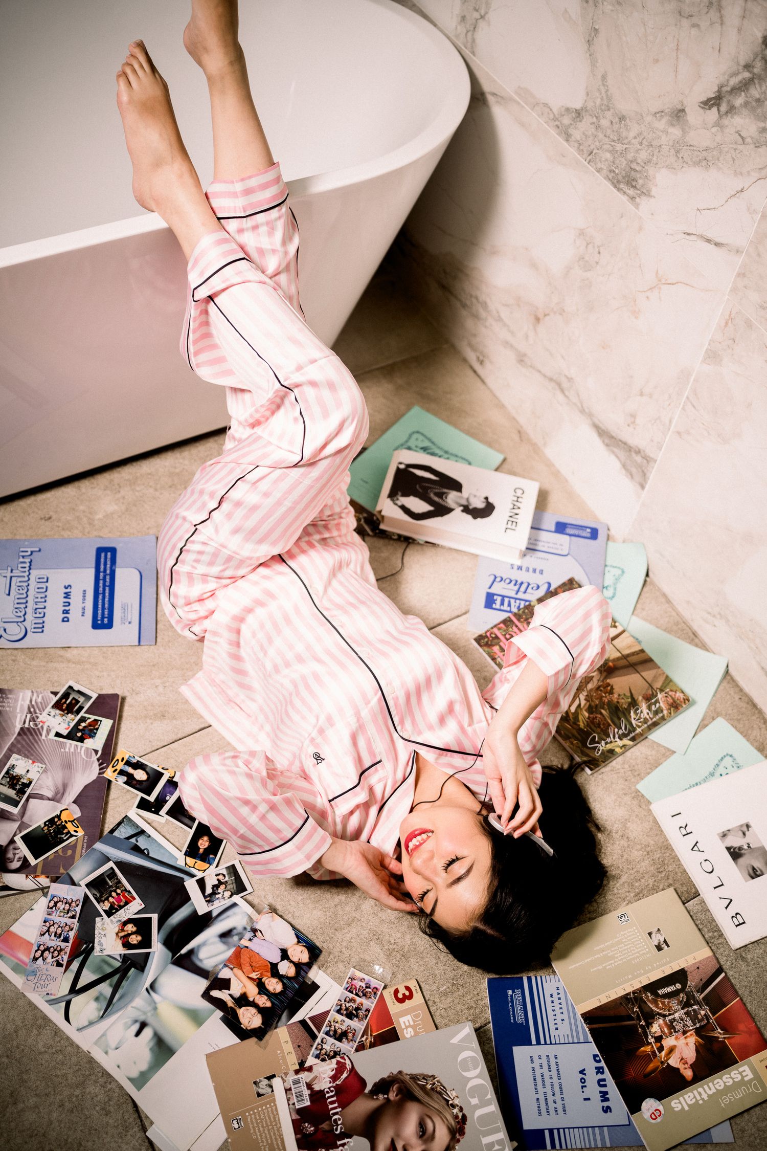 Woman in pink striped pajamas lying on bathroom floor surrounded by fashion magazines.