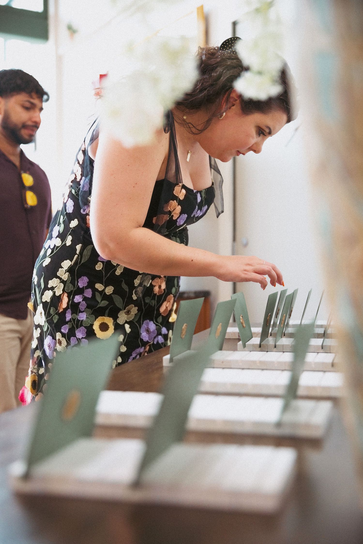 Woman in floral dress browsing place cards at a wedding reception seating display table.