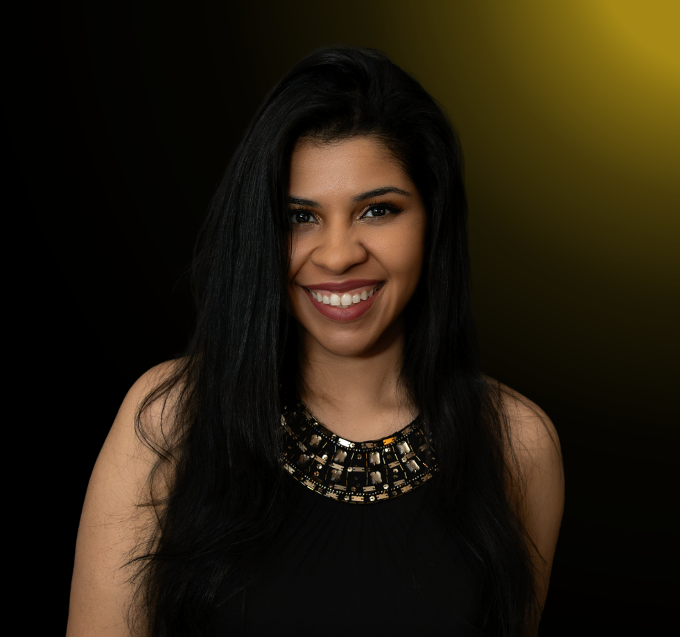 Woman in black top with statement necklace smiling against dark background in professional headshot series.