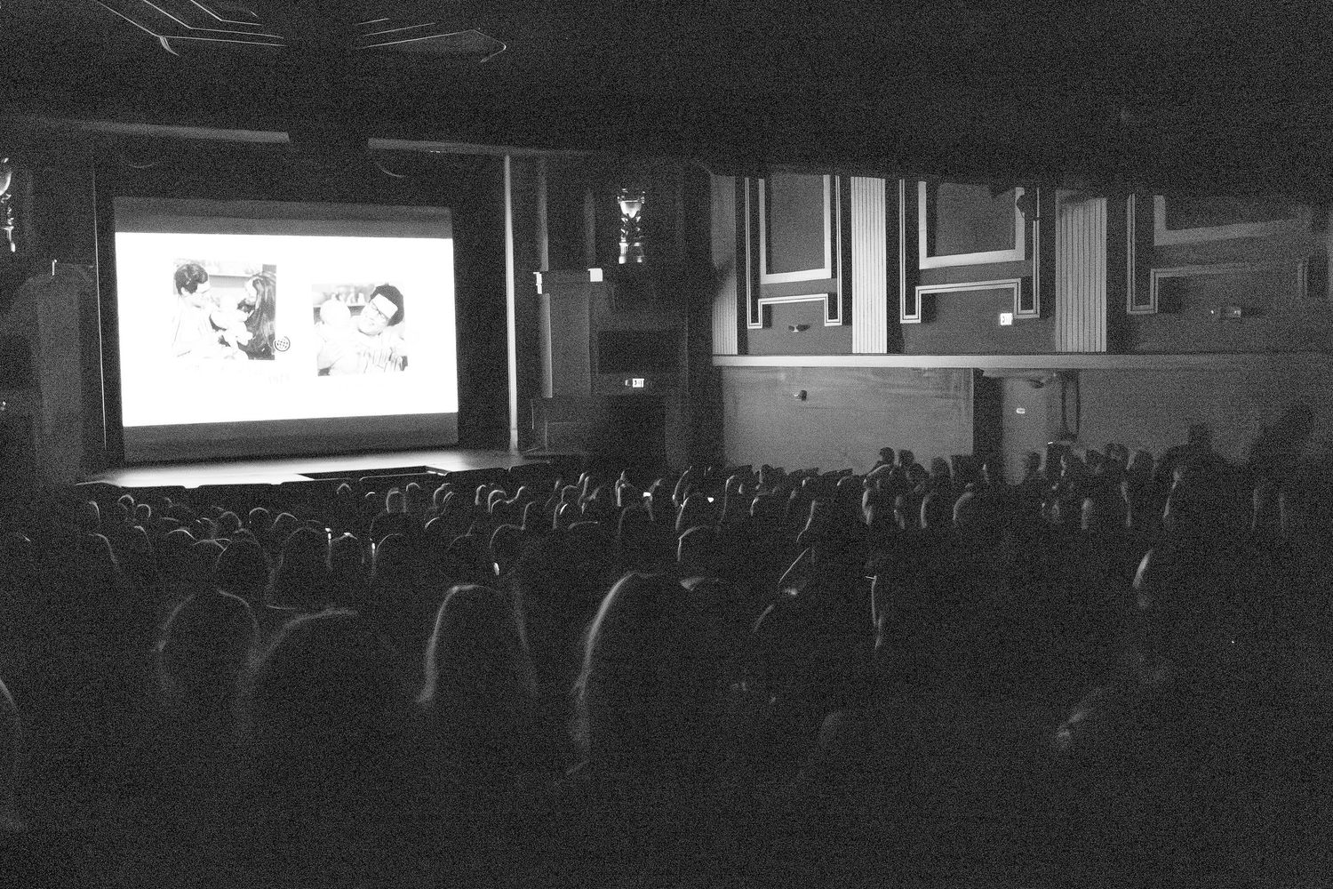 Dark panoramic view of a large audience seated in an auditorium during a presentation.
